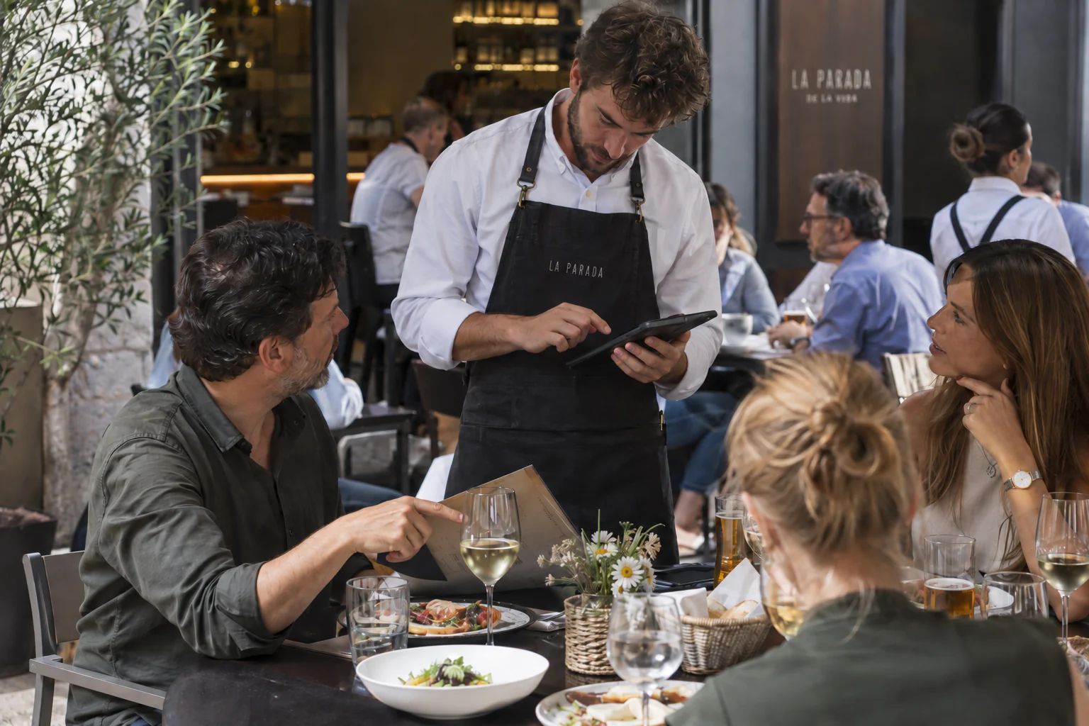 Camarero tomando una comanda con una tableta mientras atiende a los comensales